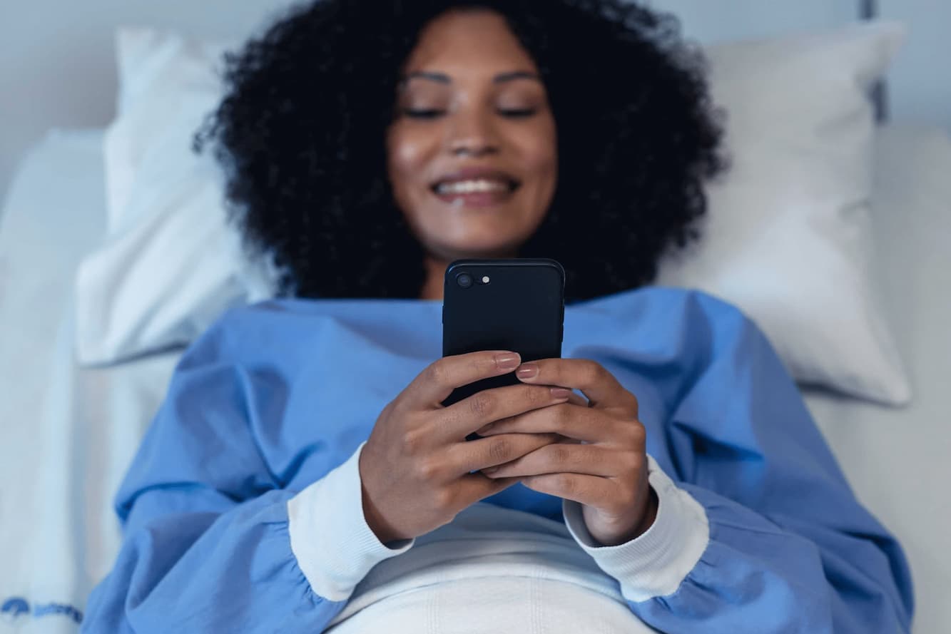 smiling patient in hospital bed holding phone 1 1